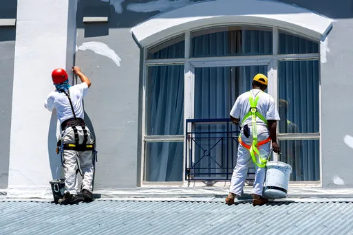 Two painters in harnesses refreshing a waterfront building facade in Newport Harbor